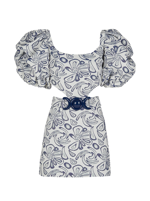 The Marlin Dress Navy Swirls from the Spring 2023 collection is a short white dress adorned with blue abstract patterns, featuring puffed sleeves and a wide navy belt with a large circular buckle.