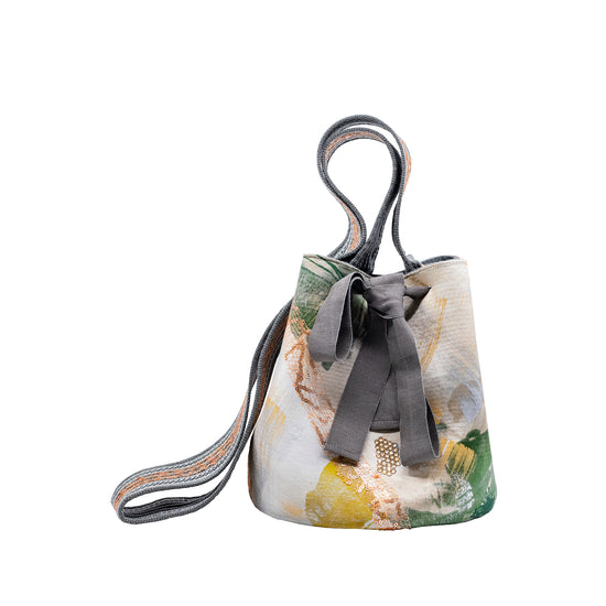 A patterned Mochila Laaput Abstract Grey handbag with a bow, featuring pastel and earth tones on a white background.